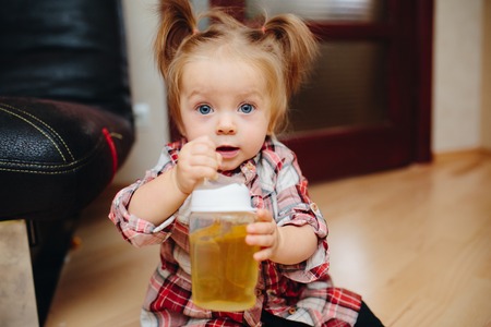 Sweet baby girl sitting on the floor and drinking teaの写真素材