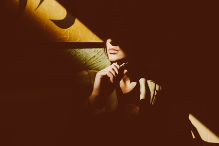 mysterious young girl sits and smokes electronic cigaretteの写真素材