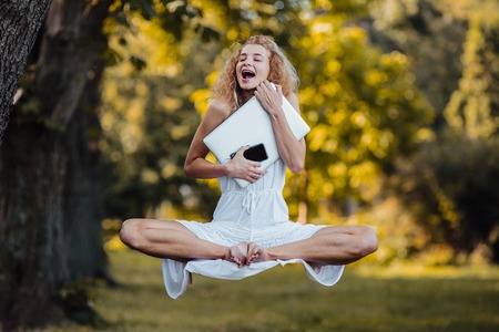 beautiful young girl levitates on nature with laptop and smartphoneの写真素材