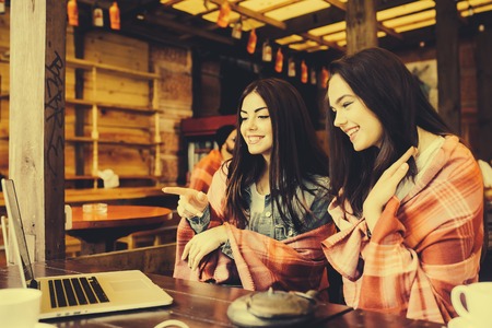 Two young and beautiful girl sitting at the table and looking for something on the Internet の写真素材
