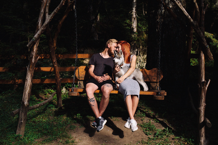 beautiful couple together with a dog resting on a swingの写真素材