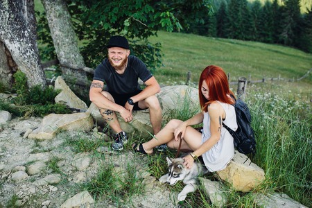beautiful couple and a dog resting on a rock beside the roadの写真素材