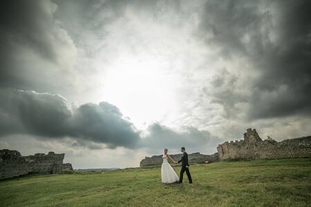 beautiful wedding couple walking on the background of the ruined castle and cloudy skyの写真素材