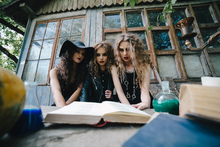 Three vintage witches perform magic ritual, at the table, reading a magical book on the eve of Halloweenの写真素材