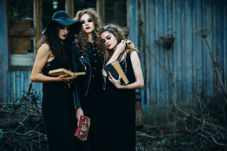 three vintage women as witches, pose in front of an abandoned building with books in hand on the eve of Halloweenの写真素材