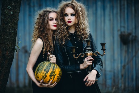 two vintage women as witches, posing in front of an abandoned house on the eve of Halloween