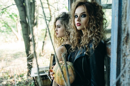 two vintage women as witches, posing beside an abandoned building on the eve of Halloweenの写真素材