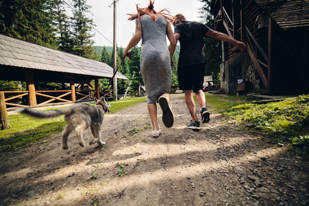couple runs on road in the nature with dog to a houseの写真素材