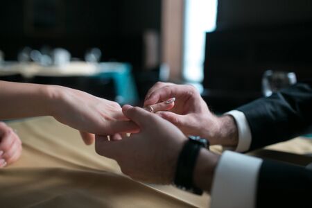 groom wears the ring bride at a table in a restaurantの写真素材
