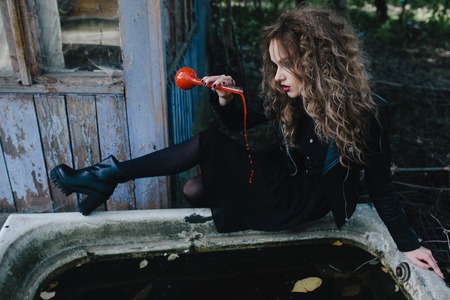 Vintage witch performs magical ritual, with elixir in hand on the eve of Halloween