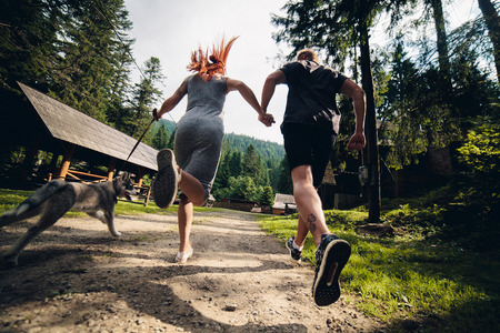 couple runs on road in the nature with dog to a houseの写真素材