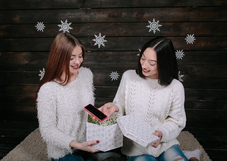 Two pretty young funny girls friends smiling and having fun, holding presents, smartfonの写真素材