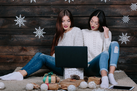 Two beautiful girls siting on the floor with a laptop, between gifts for Christmasの写真素材