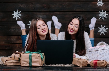 Two beautiful girls lie on the floor with a laptop, between gifts for Christmasの写真素材