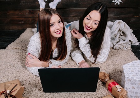 Two beautiful girls lie on the floor with a laptop, between gifts for Christmas. Looking upの写真素材