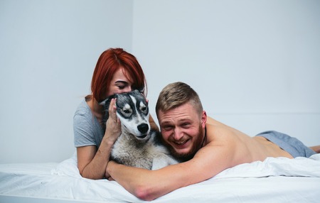 Young adult heterosexual couple lying on bed in bedroom, together with a dogの写真素材