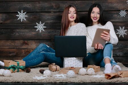 Two beautiful girls siting on the floor with a laptop and tablet, between gifts for Christmasの写真素材