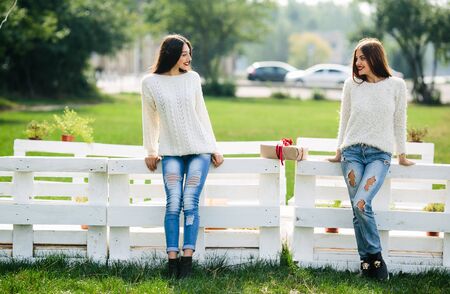 Two girls lean on a white bench in the parkの写真素材