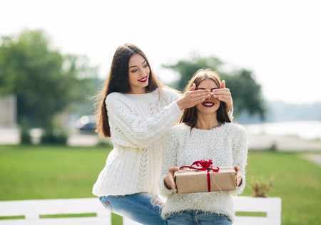 girl closes eyes with her hands the other girl with a gift