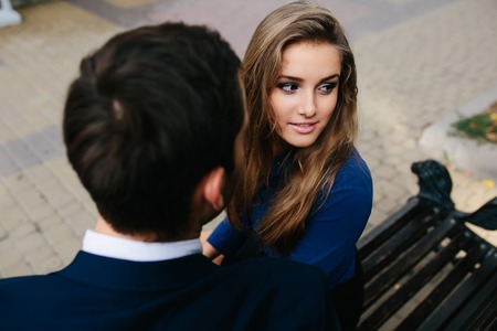 man and woman are sitting together on a bench in the old town, close angle