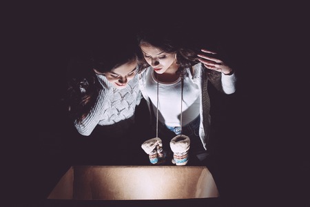 Sisters opens a box with a Christmas present and fascinated looks insideの写真素材