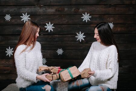 Two pretty young funny girls friends smiling and having fun, holding holiday presents, ready for celebration.の写真素材