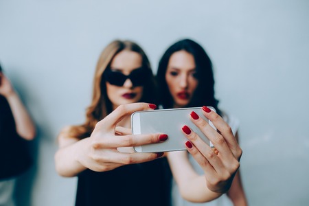 Two teenage girlfriends taking a selfie with smartphoneの写真素材