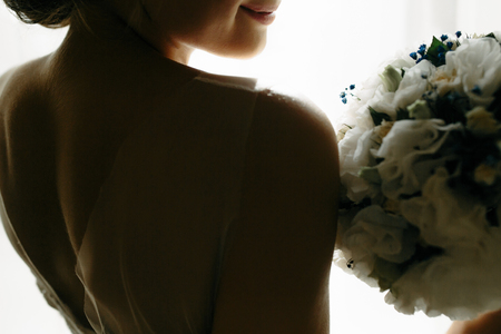 beautiful bride in a traditional white wedding dress, standing by window.の写真素材