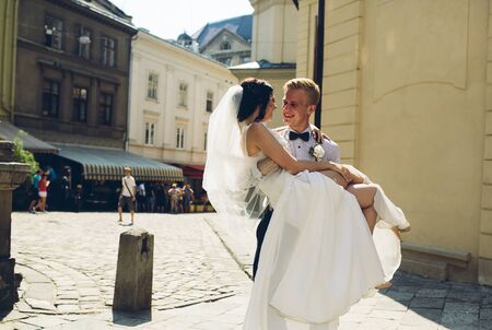 groom carries his bride in his arms through the old townの写真素材