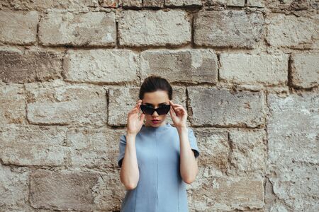 Attractive fashion woman in blue dress with sunglasses posing near white wallの写真素材
