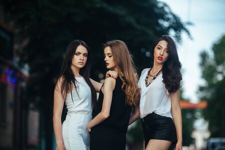 Three beautiful young girls posing on a city street at nightの写真素材
