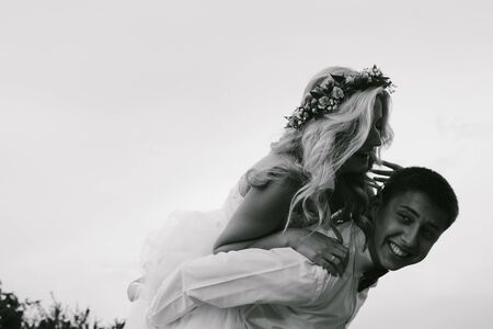 groom carries his bride on his back outdoorsの写真素材