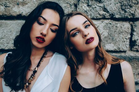 Two beautiful young girls sitting in front of an old stone wallの写真素材