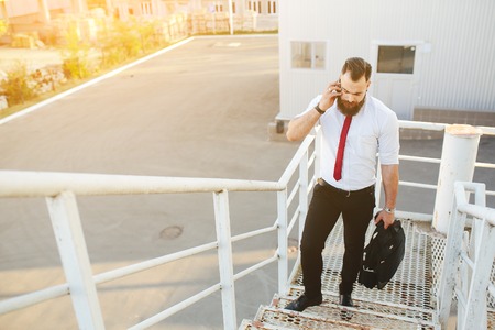 businessman stands with documents in hand and talking on the phone against a white wallの写真素材