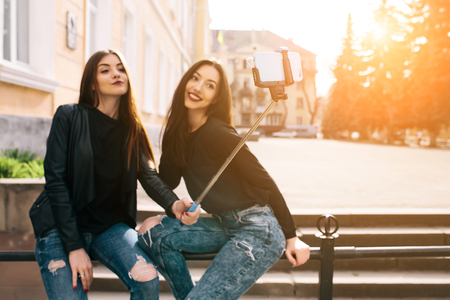 Two young adult women sitting on the bench and make selfieの写真素材