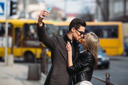 Photo of a young beautiful couple making selfie on a busy city streetの写真素材
