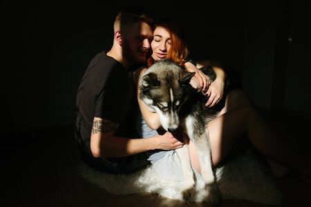 manly husband tenderly embracing his pregnant wife with a dogの写真素材