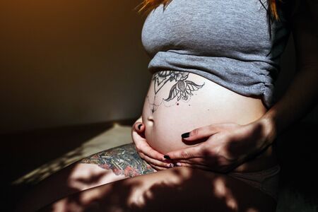 Pregnant girl posing at the camera in a dark roomの写真素材