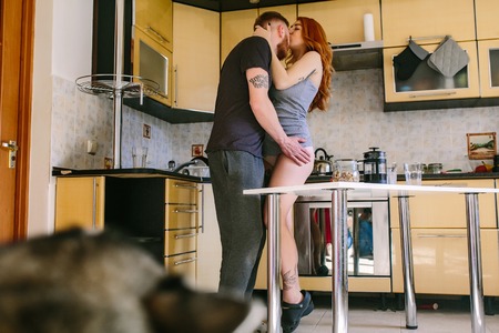 Happy pregnant woman kissing her husband with fresh fruit on the house kitchen.の写真素材
