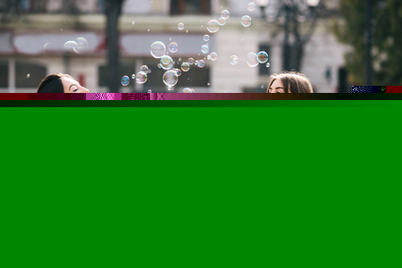 Two young adult girls sitting in a park and blow bubblesの写真素材