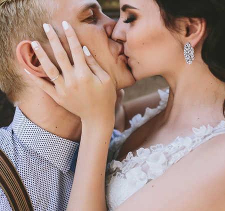 Wedding couple sitting on a stone bench and kiss each otherの写真素材
