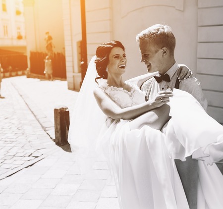 groom carries his bride in his arms through the old townの写真素材