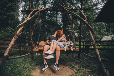 beautiful couple together with a dog resting on a swingの写真素材