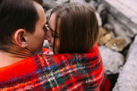 beautiful young couple sitting on a stone embankment, wrapped in a blanketの写真素材