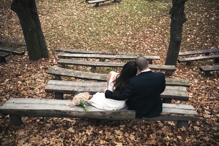 bride and groom sit on the bench in autumn parkの写真素材