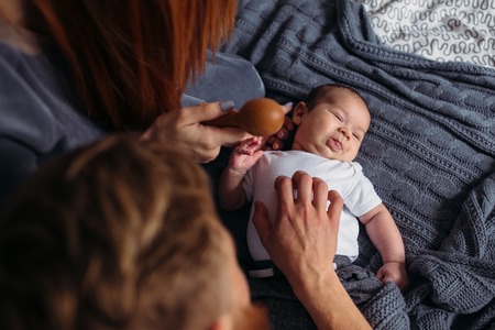 Young parents giving lots of attention to their baby. They are all sitting on a bed at home.の写真素材