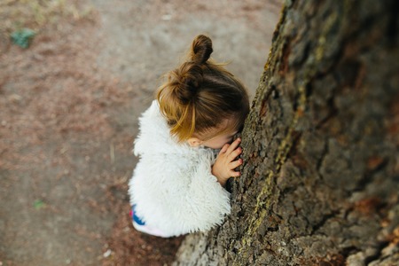 Cute little girl is playing hide and seek outdoorsの写真素材