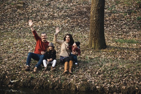 cheerful and friendly family resting on the river bank in the autumn parkの写真素材
