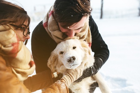 Cute young hipster couple having fun in winter park with their dog on a bright day and smilingの写真素材