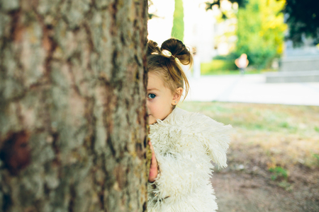 Cute little girl is playing hide and seek outdoorsの写真素材